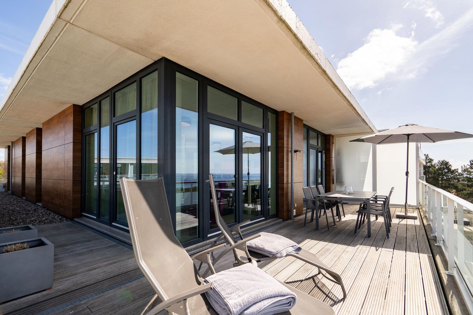 Terrasse mit Liegestühlen, Tisch und Sonnenschirm. Blick auf Meer und Himmel.