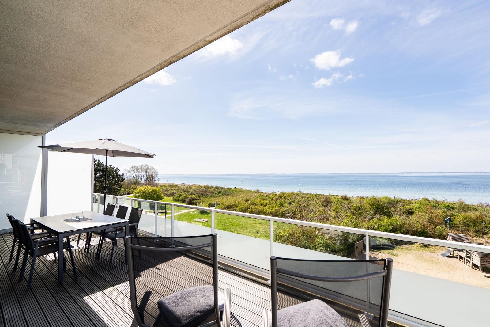 Terrasse mit Tisch, Stühlen und Sonnenschirm. Blick auf Strand und Meer.