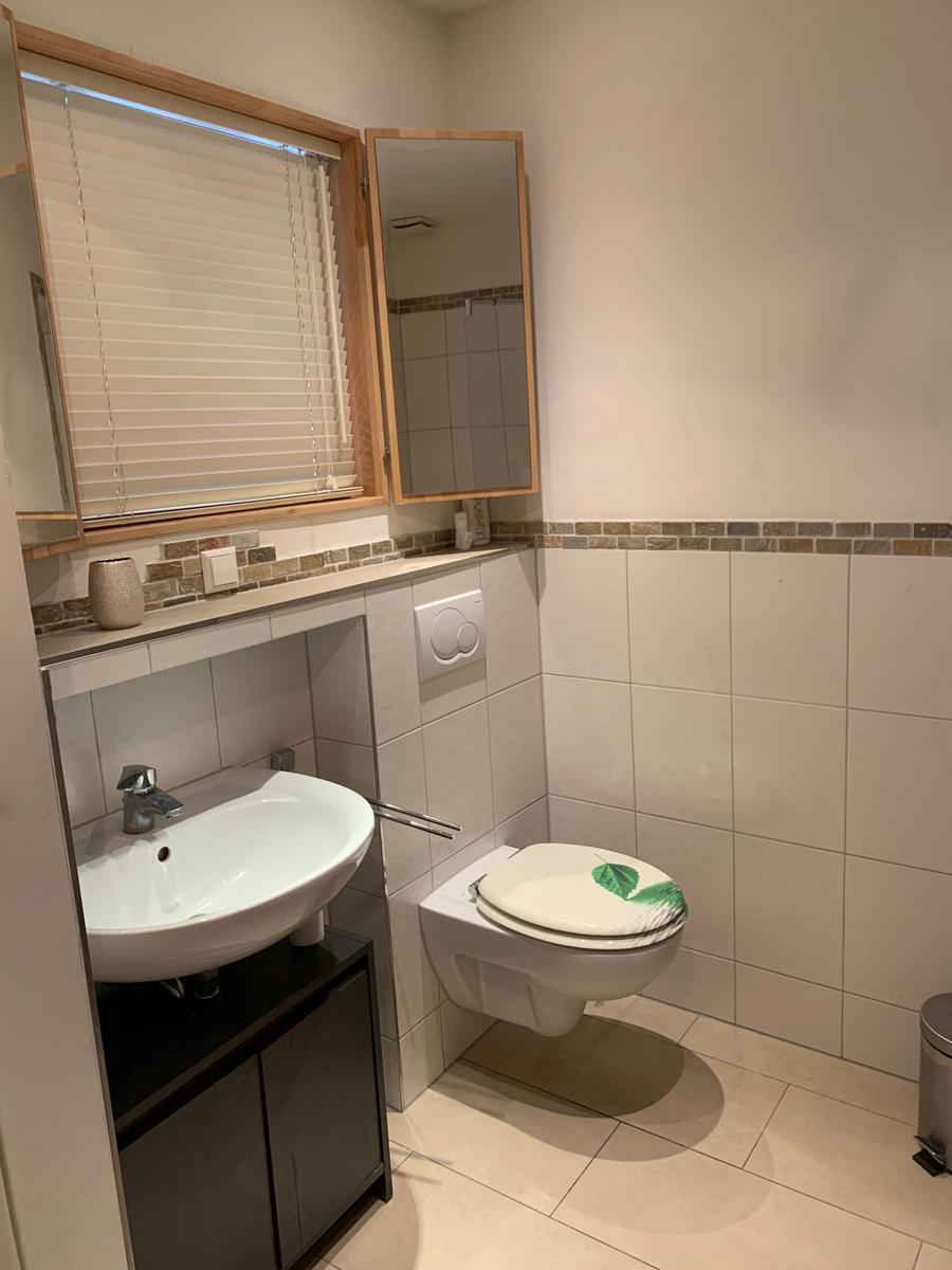 Badezimmer mit Waschbecken, Toilette und Fenster mit Jalousie.