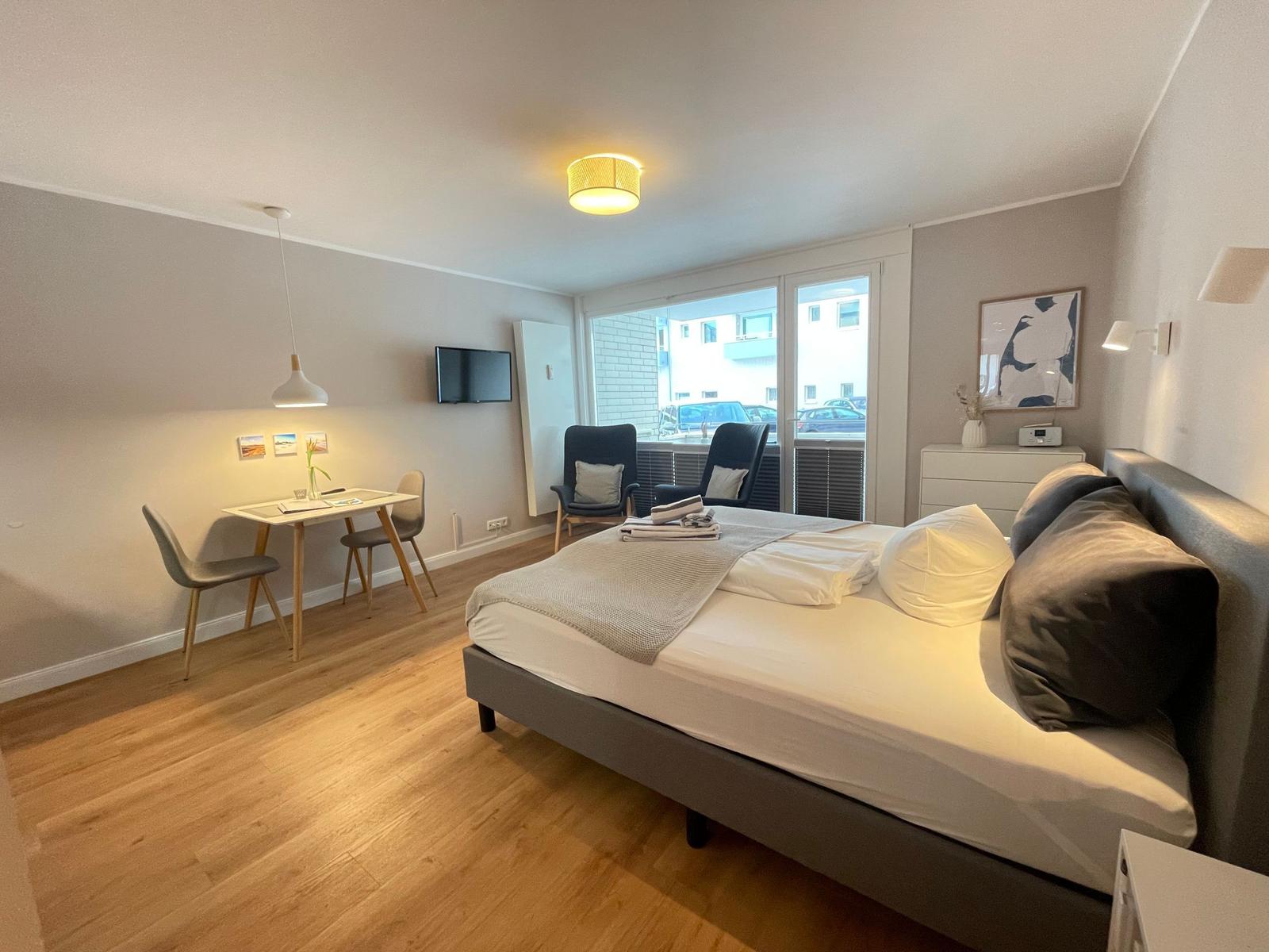 Schlafzimmer mit Bett, Schreibtisch, TV und Fenster zur Straße.