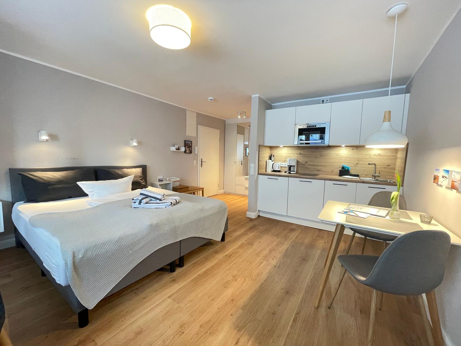 Schlafzimmer mit Bett, Küche und Esstisch mit Stühlen.