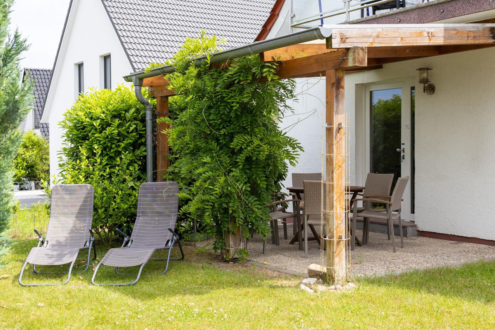 Terrasse mit Tisch, Stühlen und Sonnenliegen. Grüner Garten mit Pergola und Hecke.