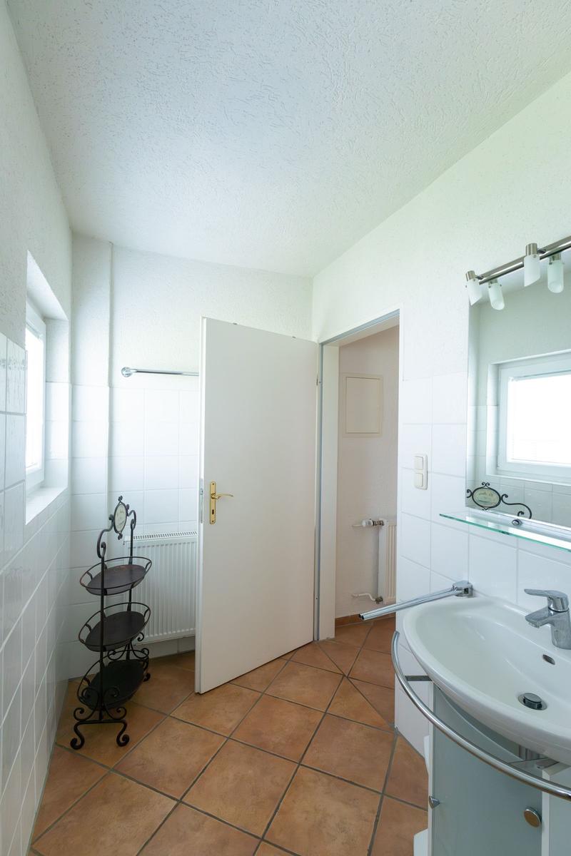 Badezimmer mit Waschbecken, Spiegel und Tür zum Duschbereich.