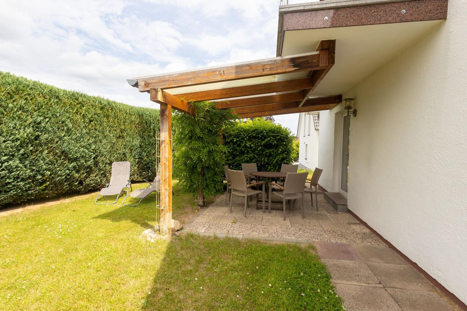 Terrasse mit Tisch, Stühlen und Sonnenschutz unter einem Holzvordach.