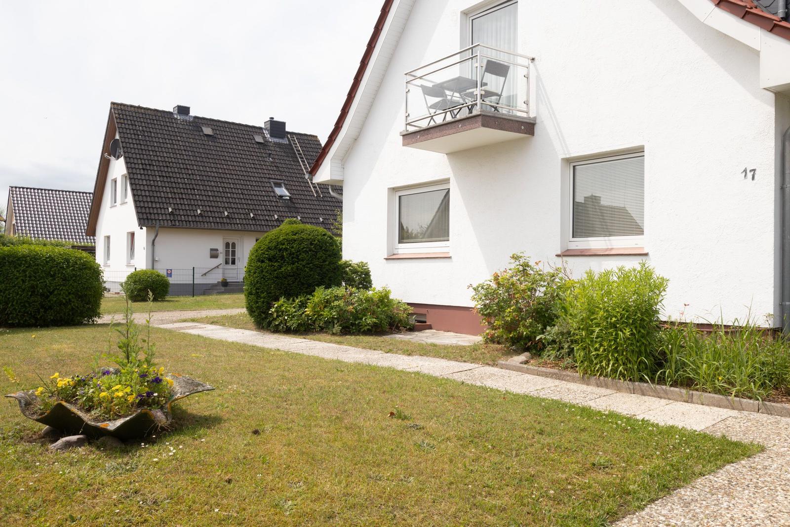Wohnhaus mit Balkon, Gartenweg und Beet mit Blumen.