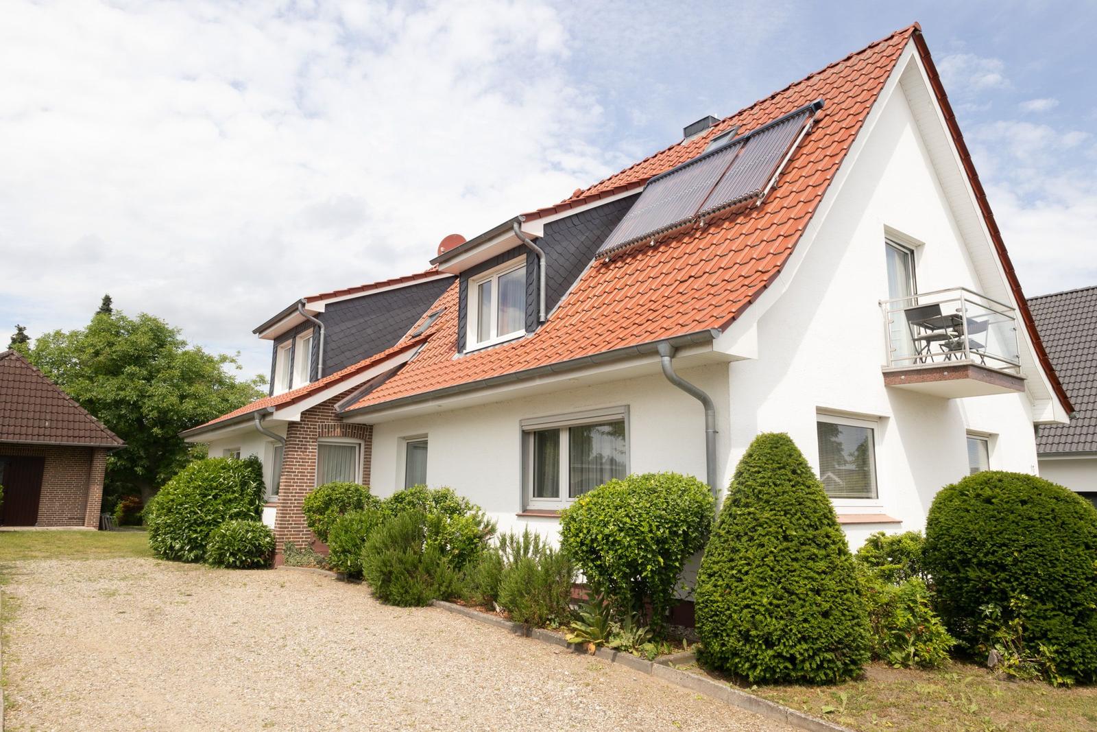 Ein weißes Haus mit rotem Dach, Balkon und gepflegtem Garten.