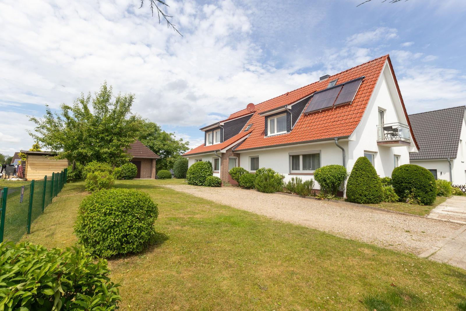Wohnhaus mit rotem Dach, Balkon und gepflegtem Garten mit Rasen und Sträuchern.