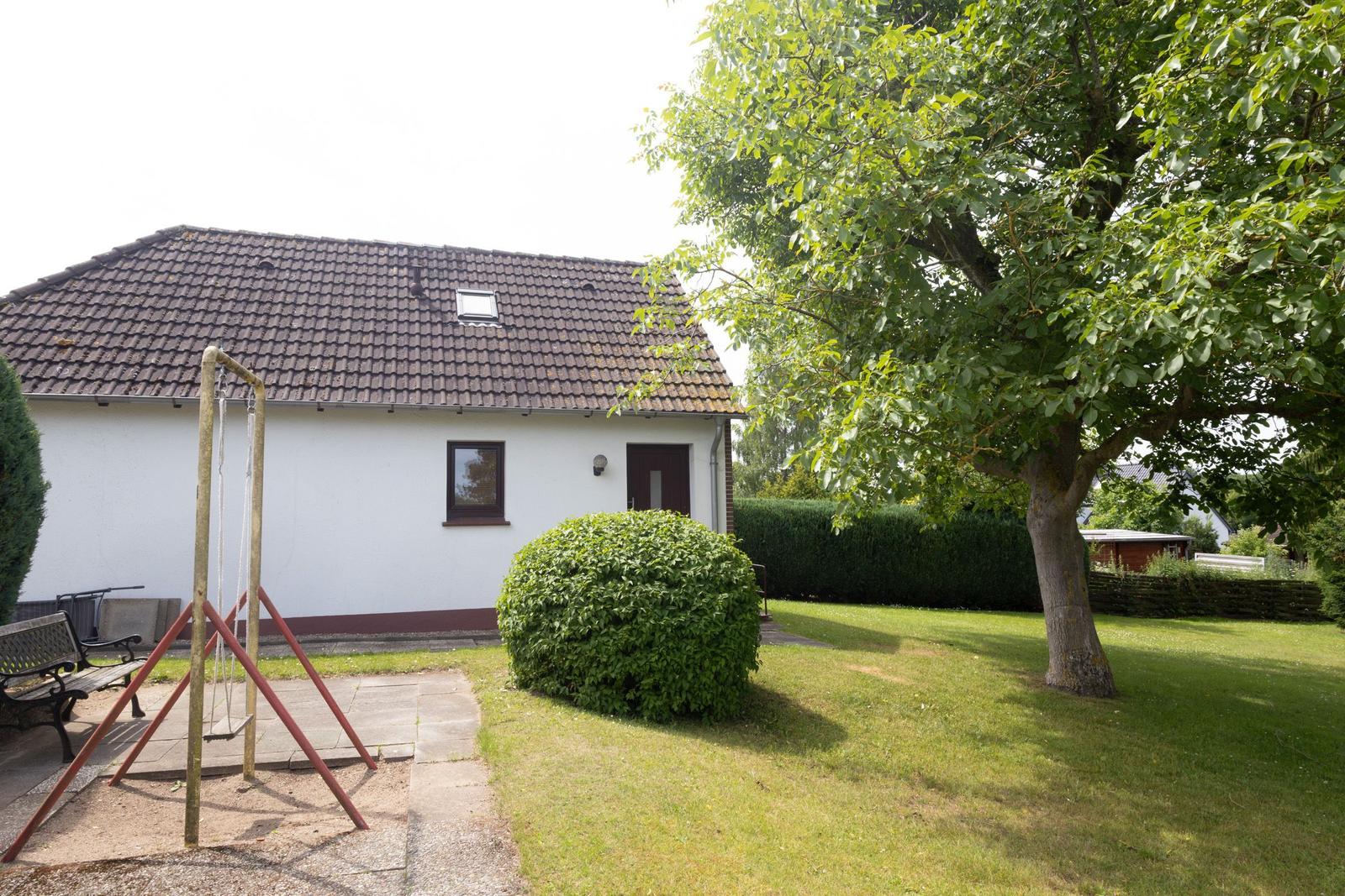 Ein weißes Haus mit Garten, Schaukel und Baum. Die Fassade ist weiß, mit dunklen Fenstern und Tür.