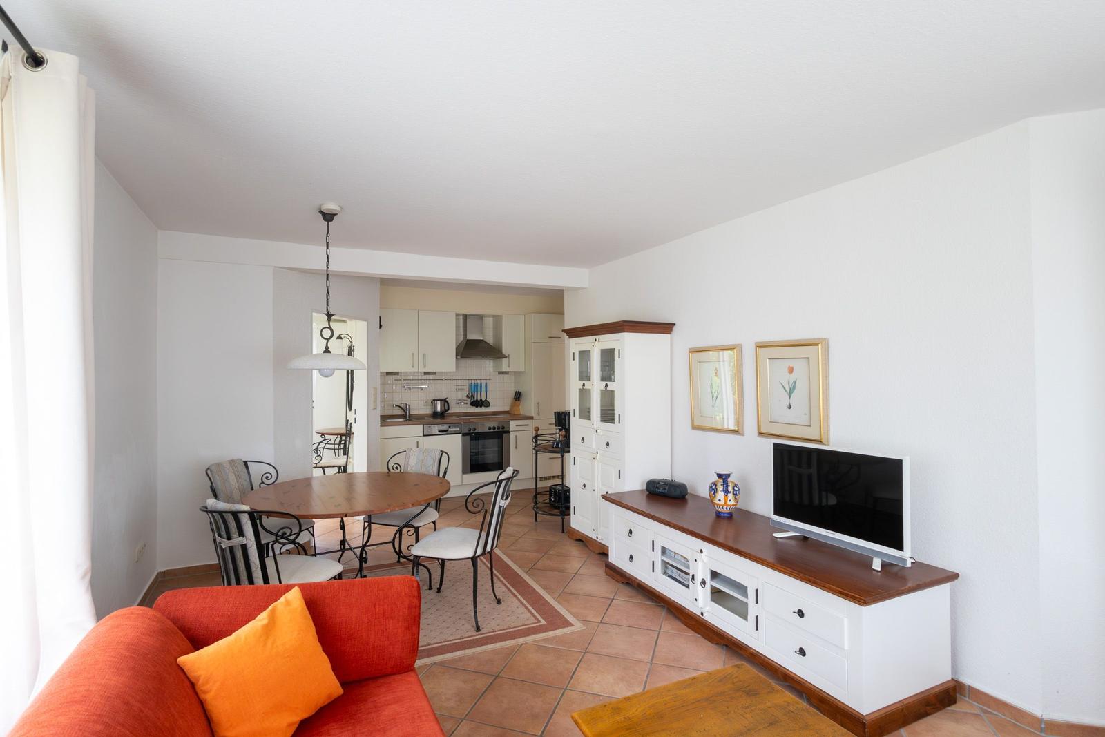 Wohn- und Essbereich mit Küche, Sofa, TV und Esstisch.