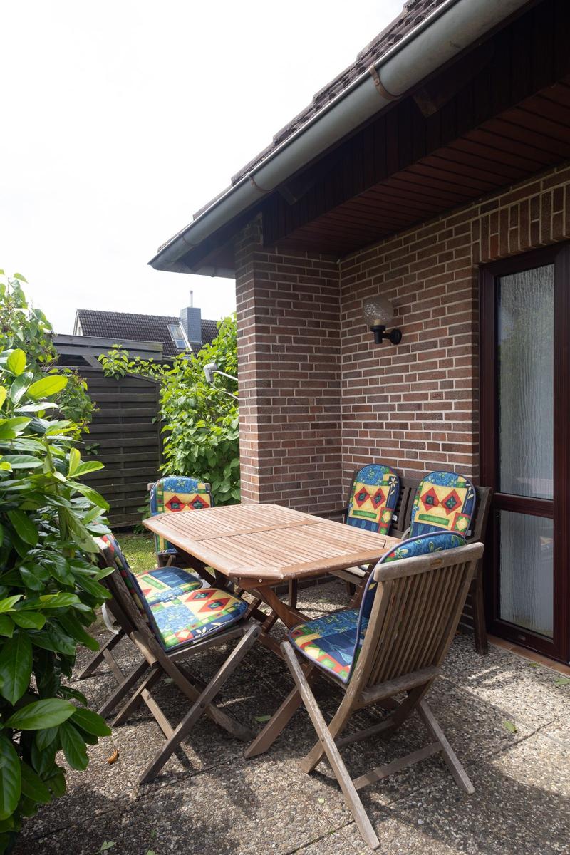 Terrasse mit Holztisch und vier Stühlen mit bunten Sitzkissen.