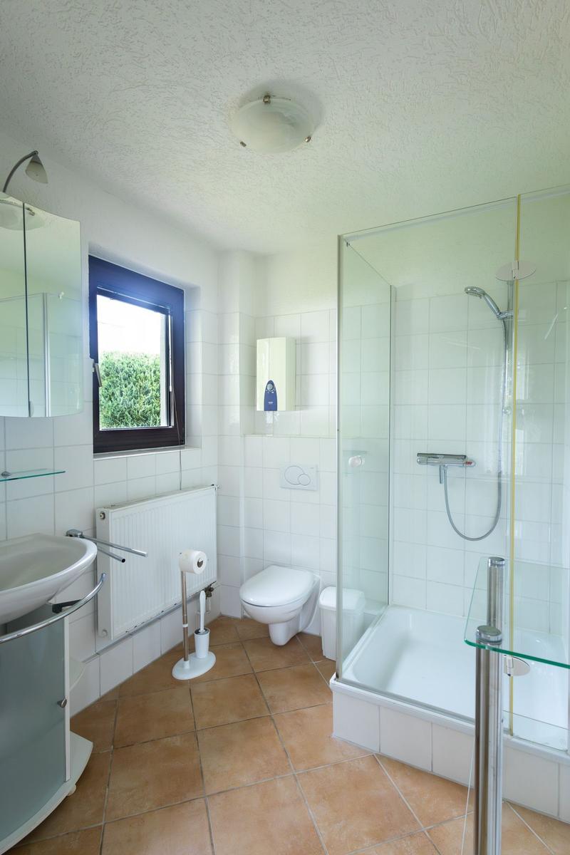 Badezimmer mit Dusche, Toilette und Waschbecken. Fenster mit Blick auf Grün.