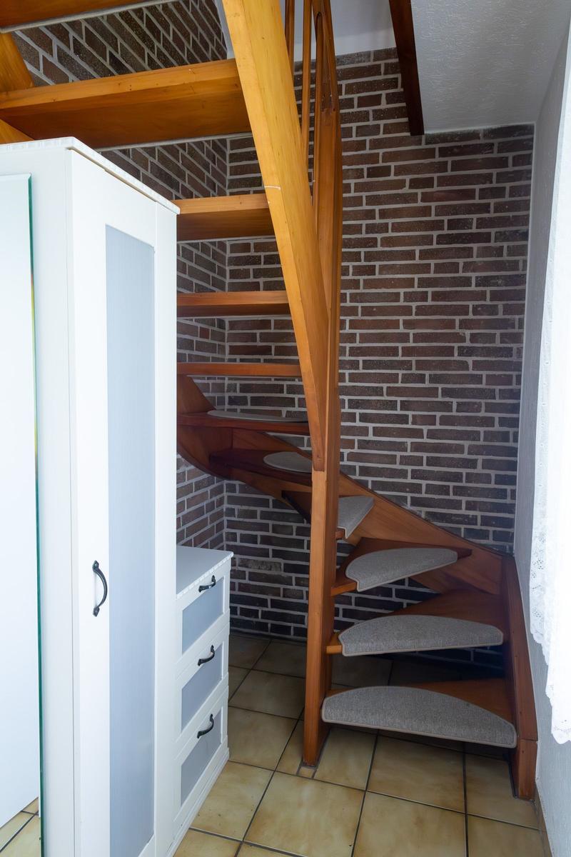 Holzspiralstiege mit gepolsterten Stufen neben weißem Schrank und Ziegelwand.