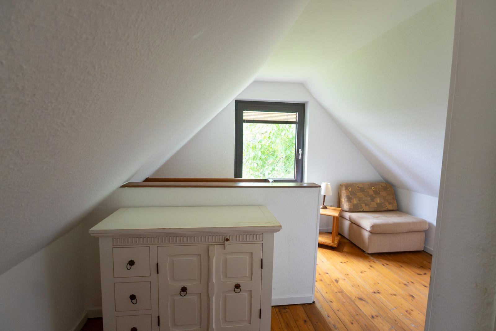 Zimmer mit Dachschrägen, Fenster, Schrank und Sitzbank auf Holzboden.