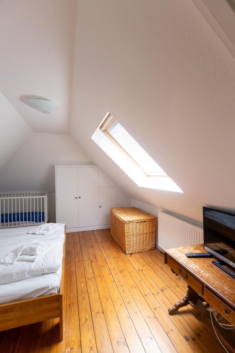 Dachgeschosszimmer mit Dachschräge, Dachfenster, Bett, Kleiderschrank und Holzboden.