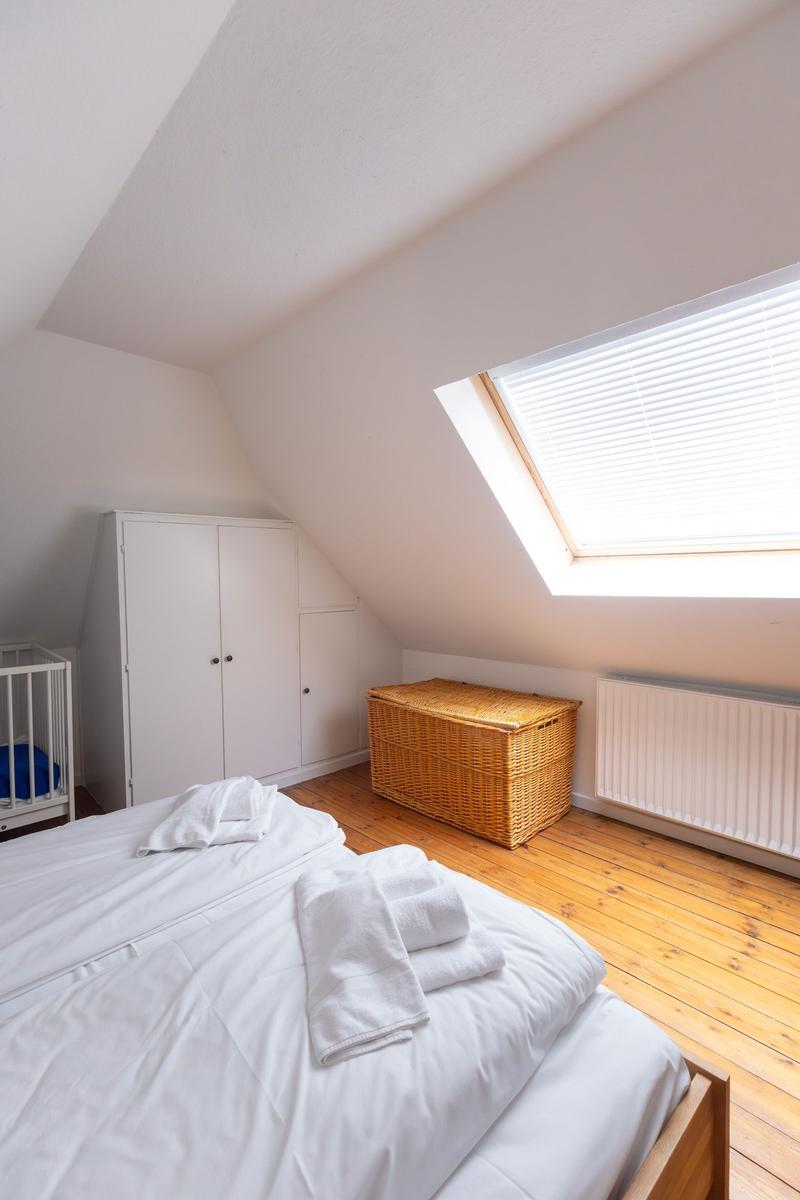Schlafzimmer mit Dachschräge, Dachfenster, Holzboden, Bett, Wickelkommode und Korb.
