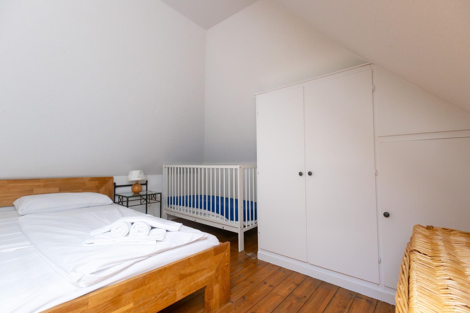 Schlafzimmer mit Doppelbett, Kinderbett und Kleiderschrank unter Dachschrägen.