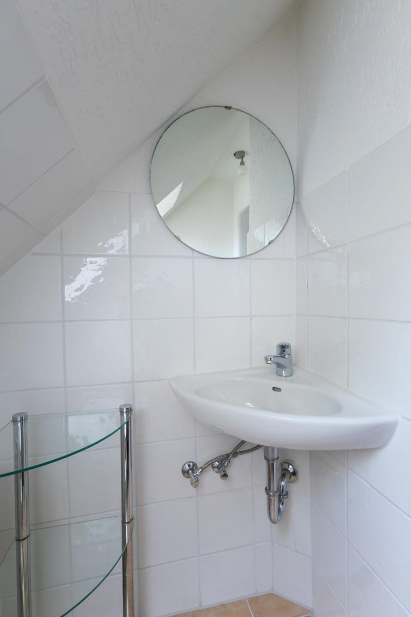 Badezimmer mit weißer Wandfliese, runder Spiegelfläche und eingebauter Waschschale.