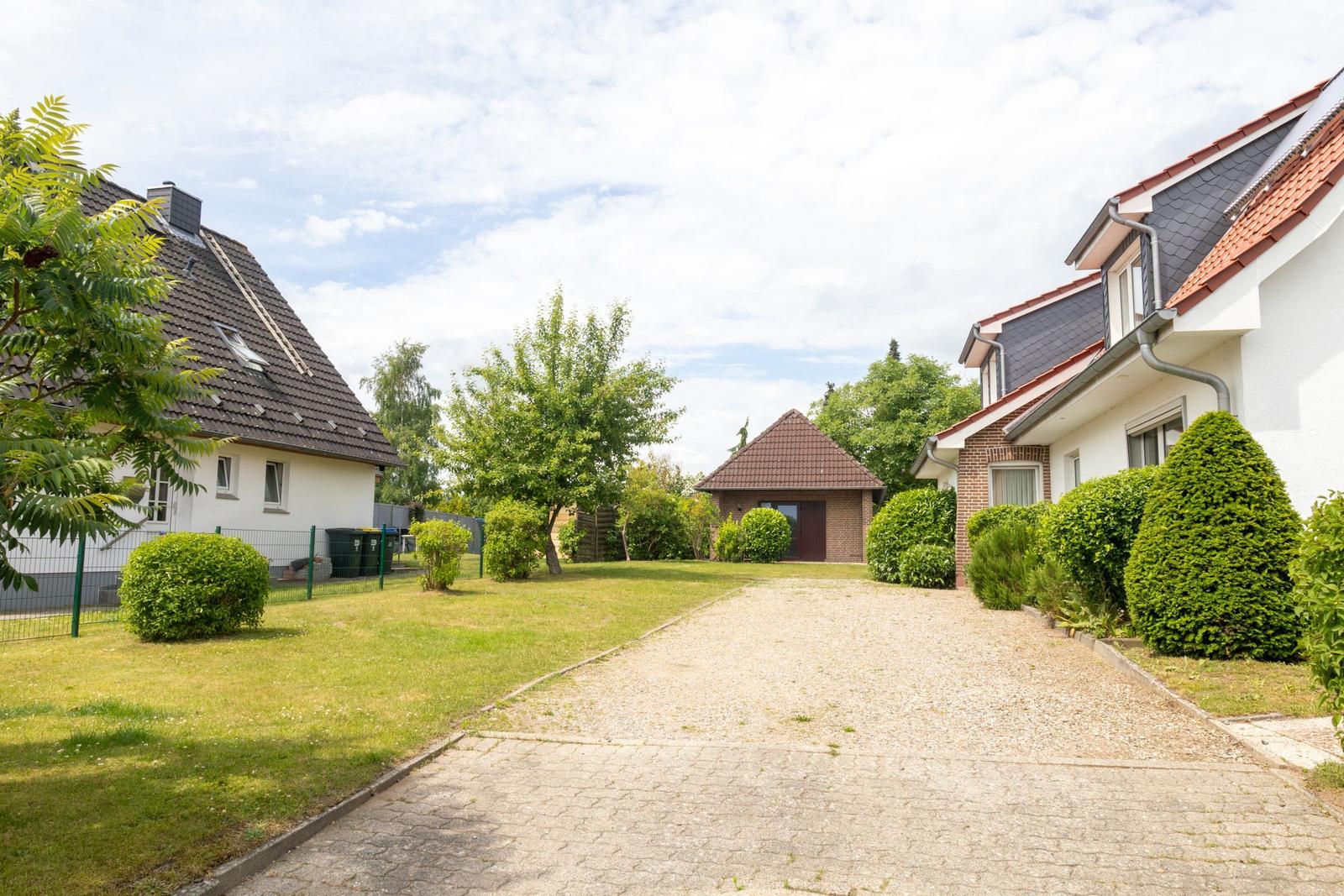 Haus mit gepflastertem Weg, Grünflächen und Bäumen im Vorgarten.