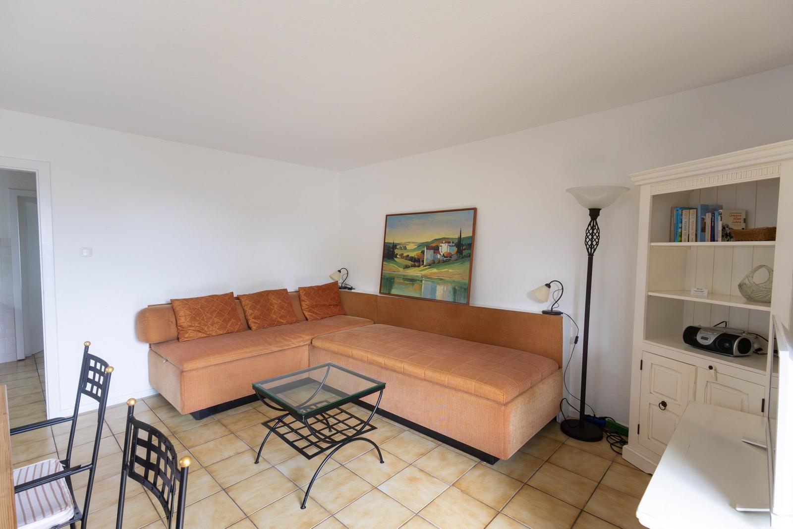 Wohnzimmer mit Ecksofa, Glas-Tisch und Bücherregal an der Wand.