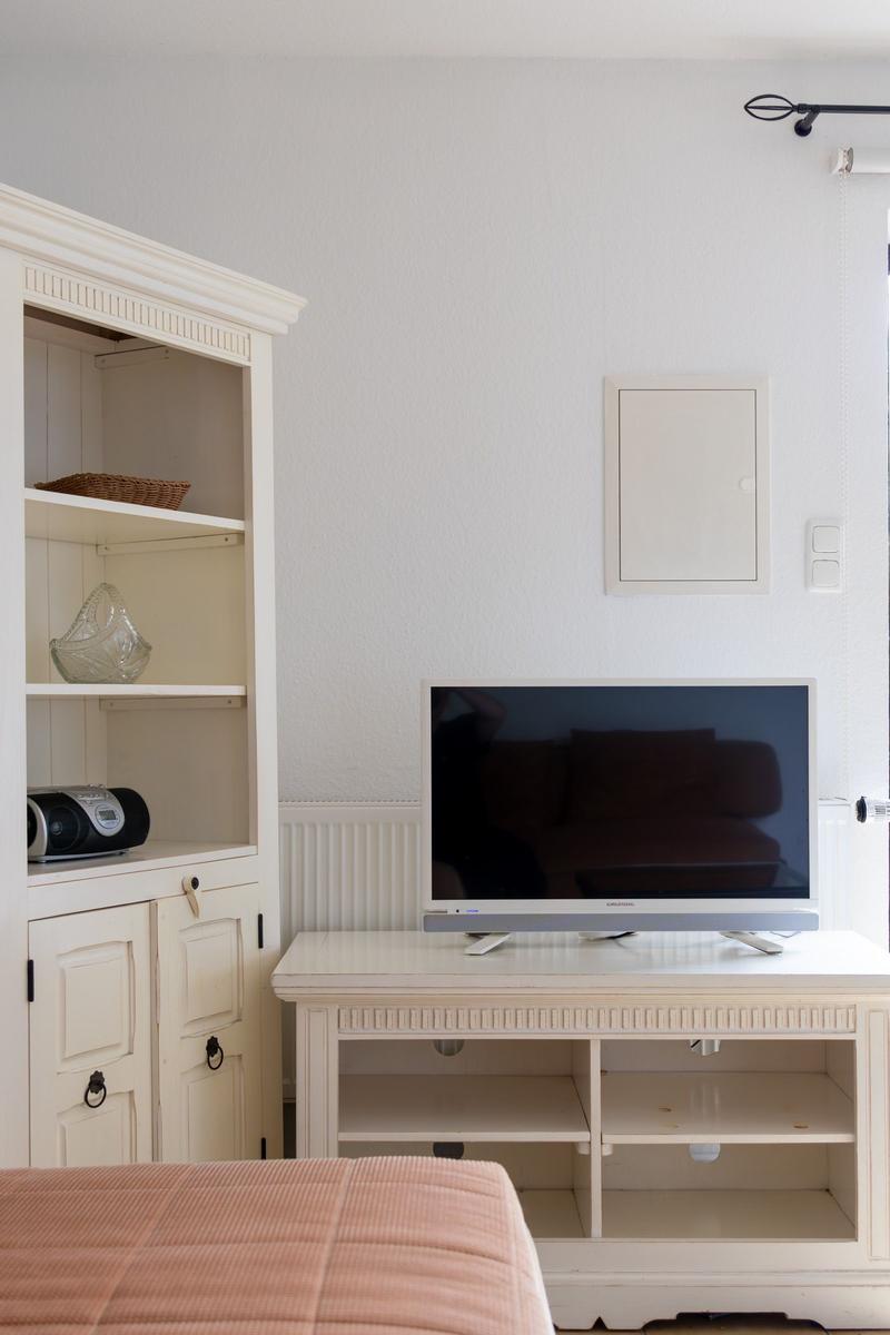 Ein Raum mit einem Fernseher auf einem weißen Schrank und einem weißen Sideboard mit offenen Fächern.