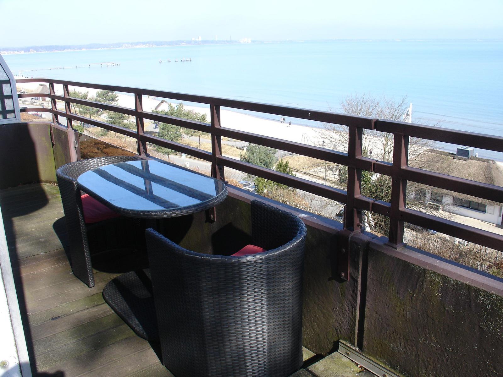 Terrasse mit Tisch und Stühlen, Blick auf Strand und Meer.