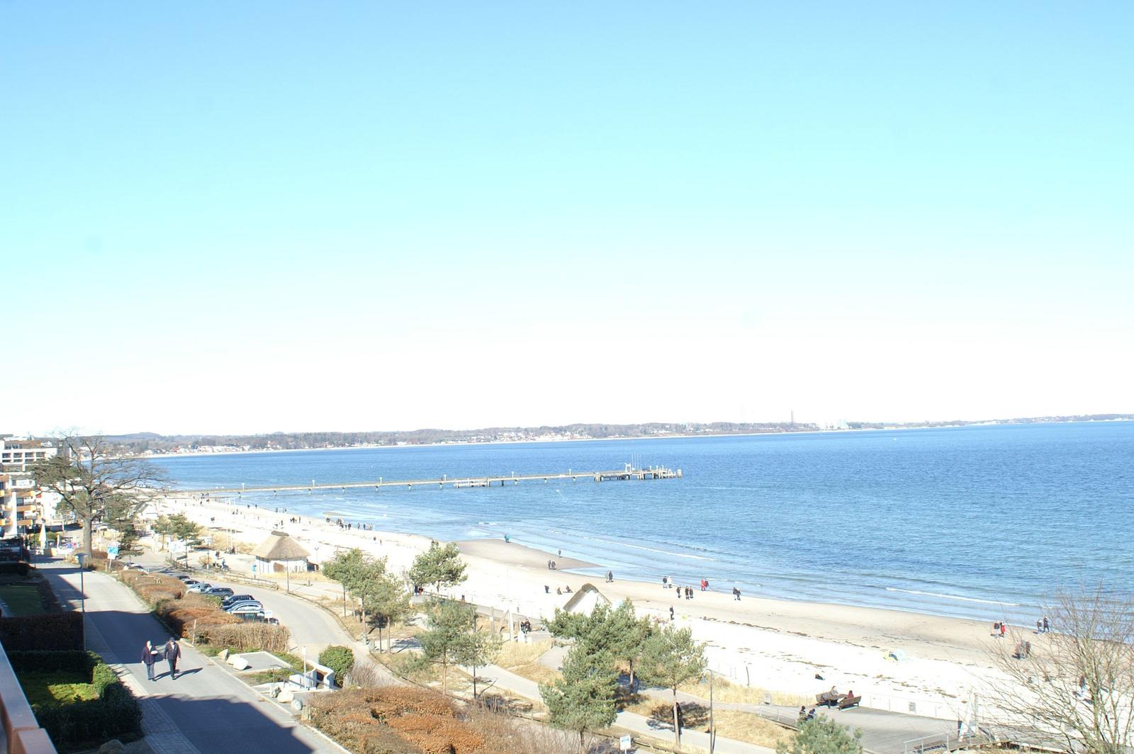 Blick auf einen Strand mit Promenade und Steg über das Wasser.
