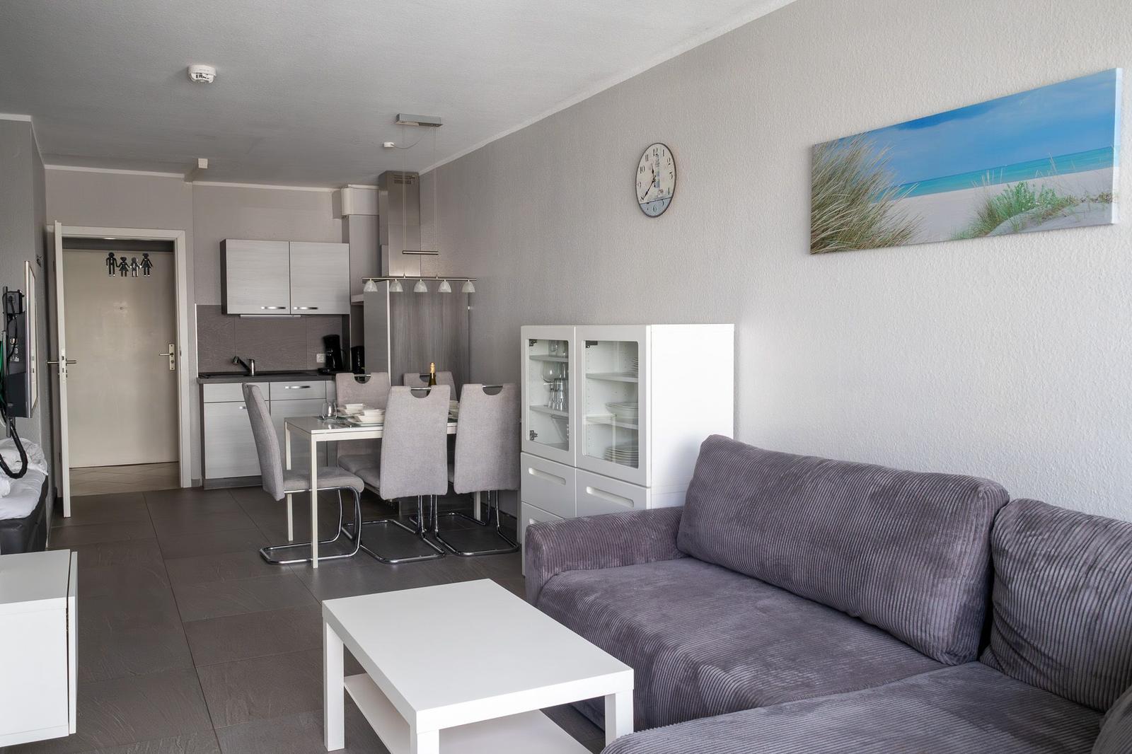 Wohnzimmer mit Sofa, Esstisch und Küche im Hintergrund.