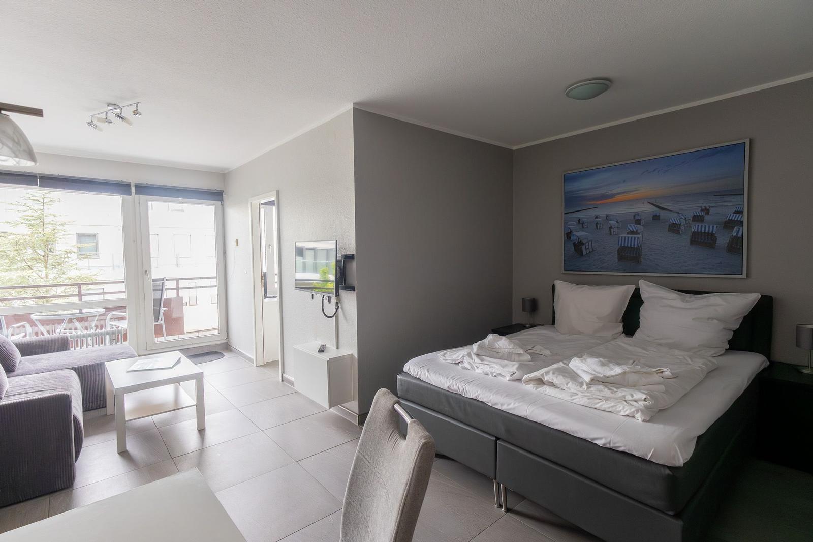 Schlafzimmer mit Bett, Wandbild und TV. Wohnbereich mit Sofa, Tisch und Balkon.
