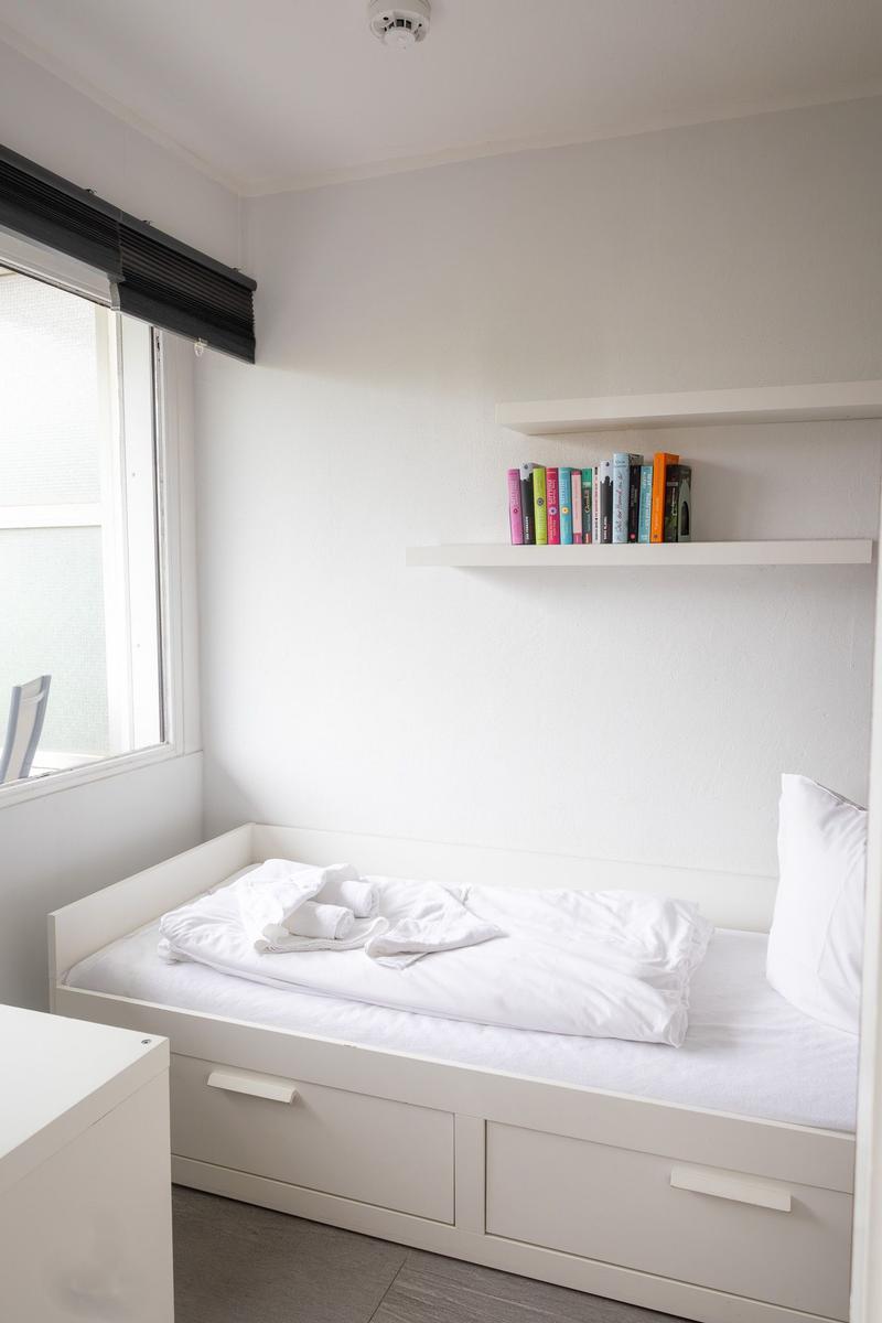 Schlafzimmer mit weißem Bett, Regal mit Büchern und Fenster