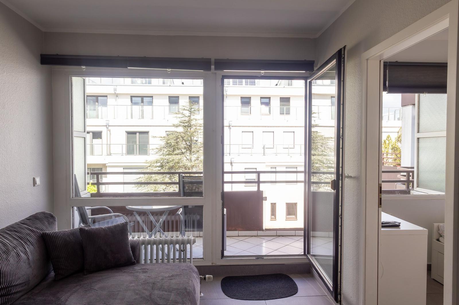 Wohnraum mit Blick auf Balkon und gegenüberliegendes Gebäude.