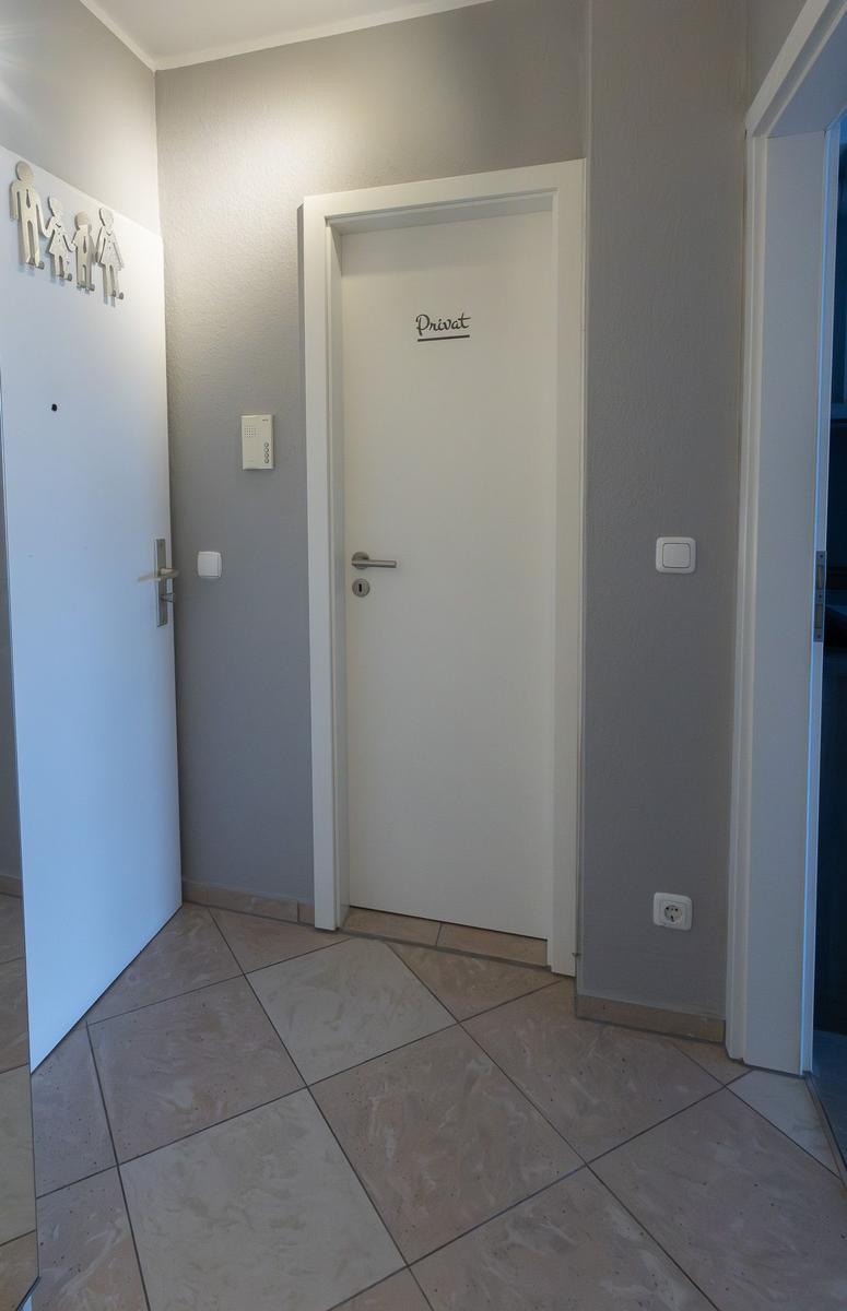 Flur mit Tür zur privaten Wohnung und Toilettenzeichen an der Wand.