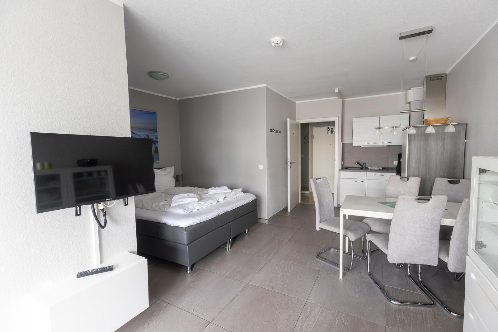 Schlafzimmer mit Bett, Fernseher und angrenzender Küche mit Esstisch.