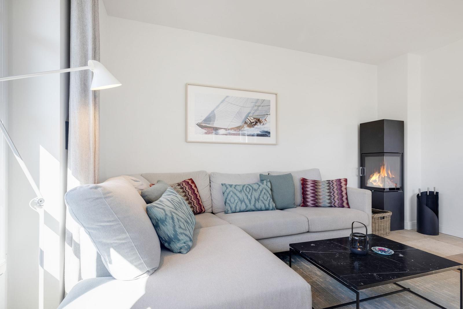 Ein Wohnzimmer mit Sofa, Kamin und Tisch. Wandbild zeigt Segelyacht.