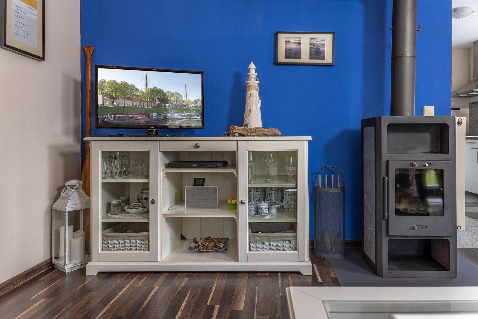 Ein Wohnzimmer mit Fernseher, Schrank und Kaminofen an blauer Wand.