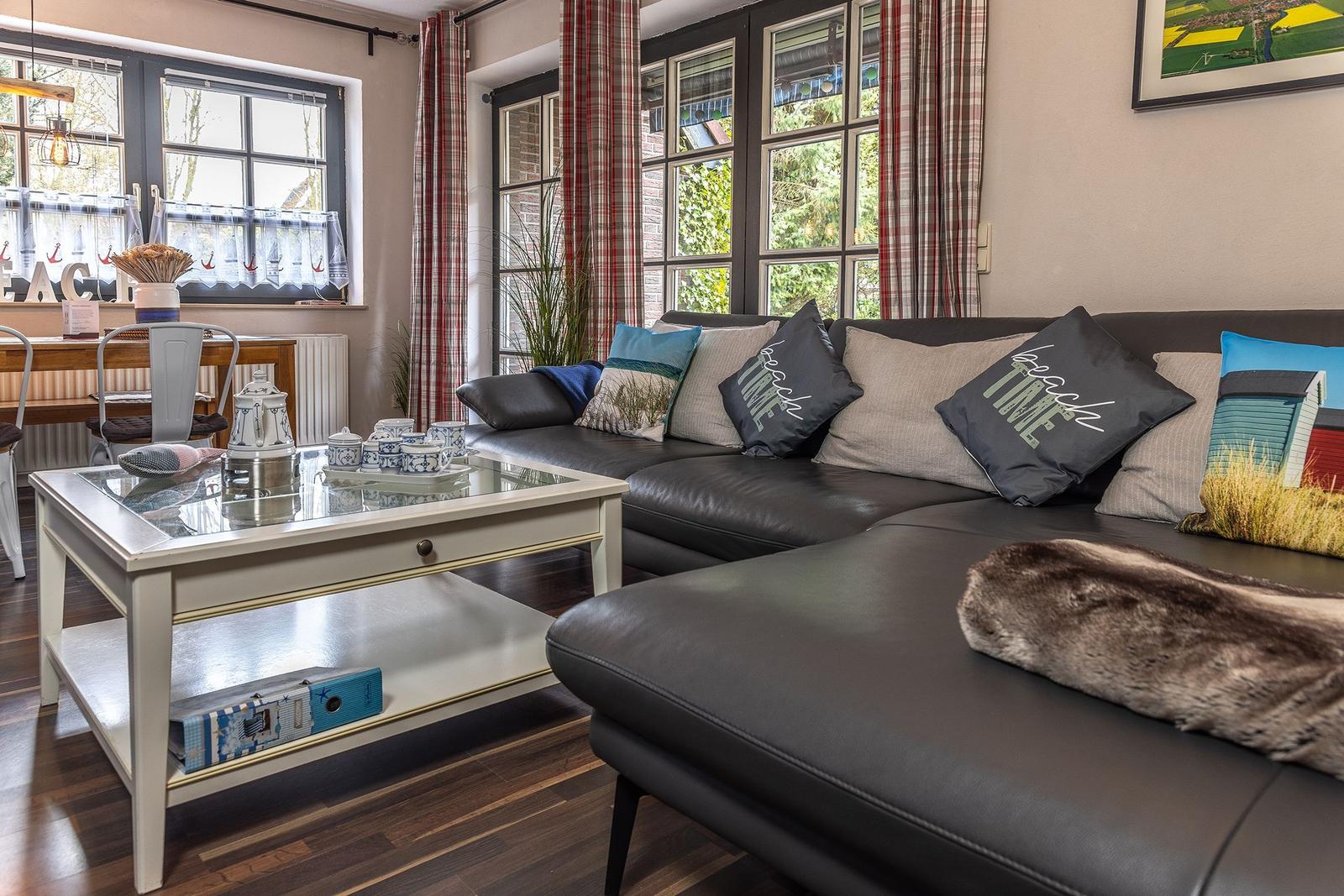 Ein Wohnzimmer mit einem schwarzen Sofa, einem weißen Couchtisch und großen Fenstern.