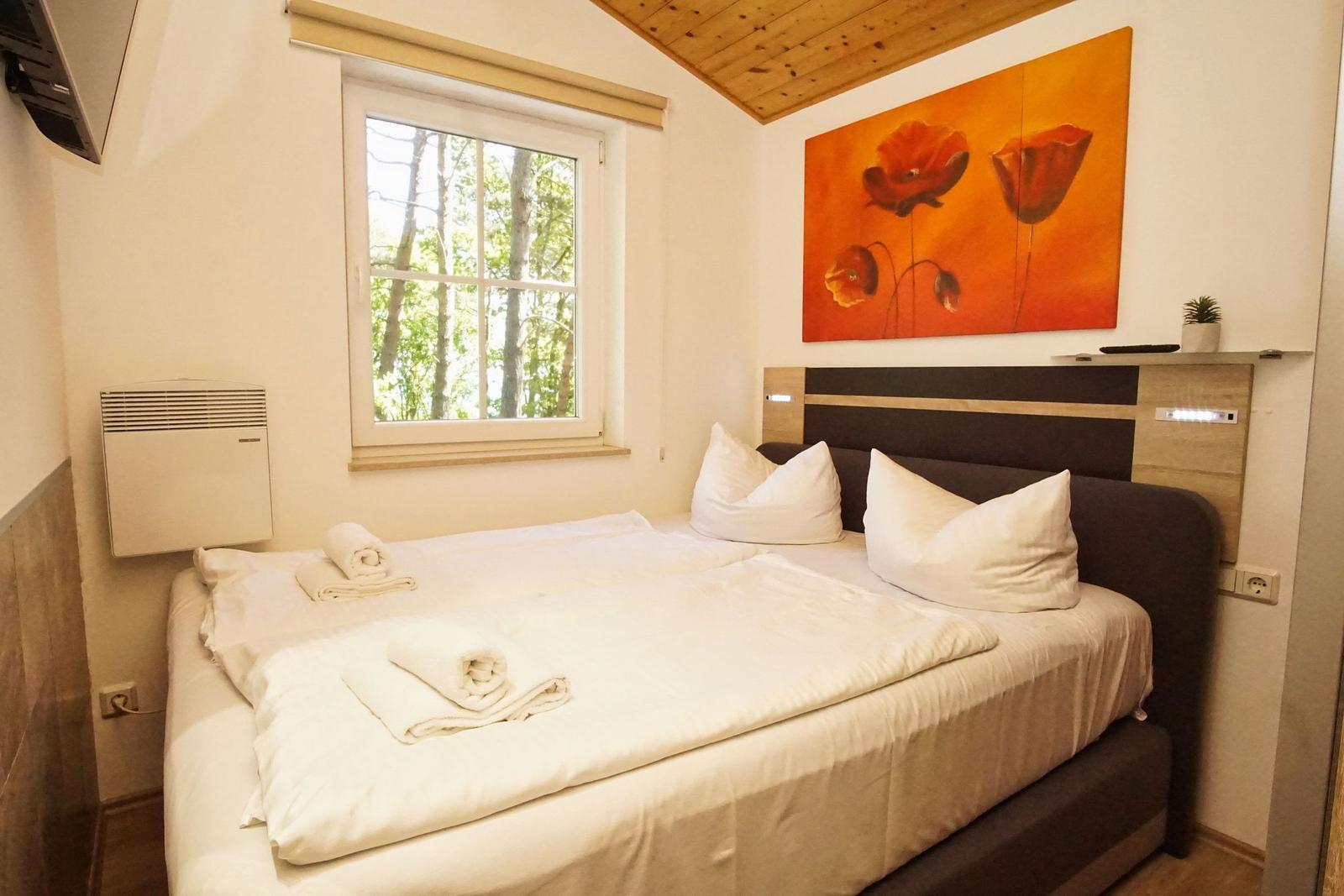 Schlafzimmer mit Doppelbett, Fenster zum Wald und Wandbild mit roten Mohnblumen.