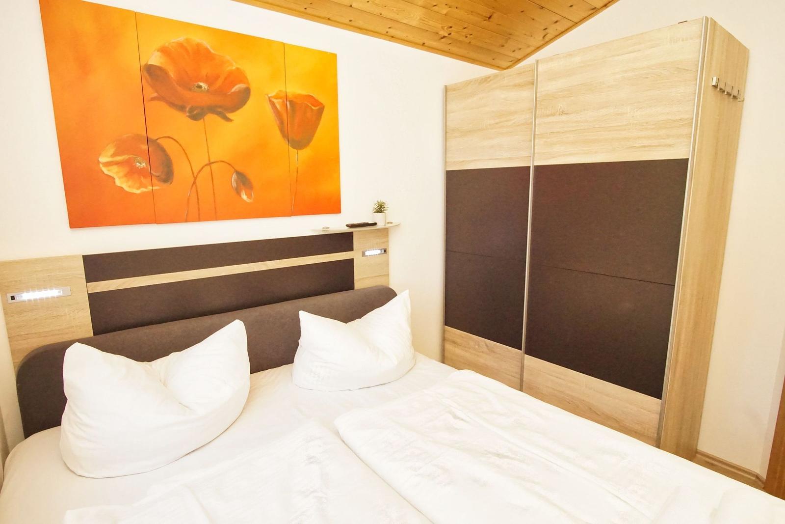 Schlafzimmer mit Bett, Kleiderschrank und Wandbild mit Mohnblumen.