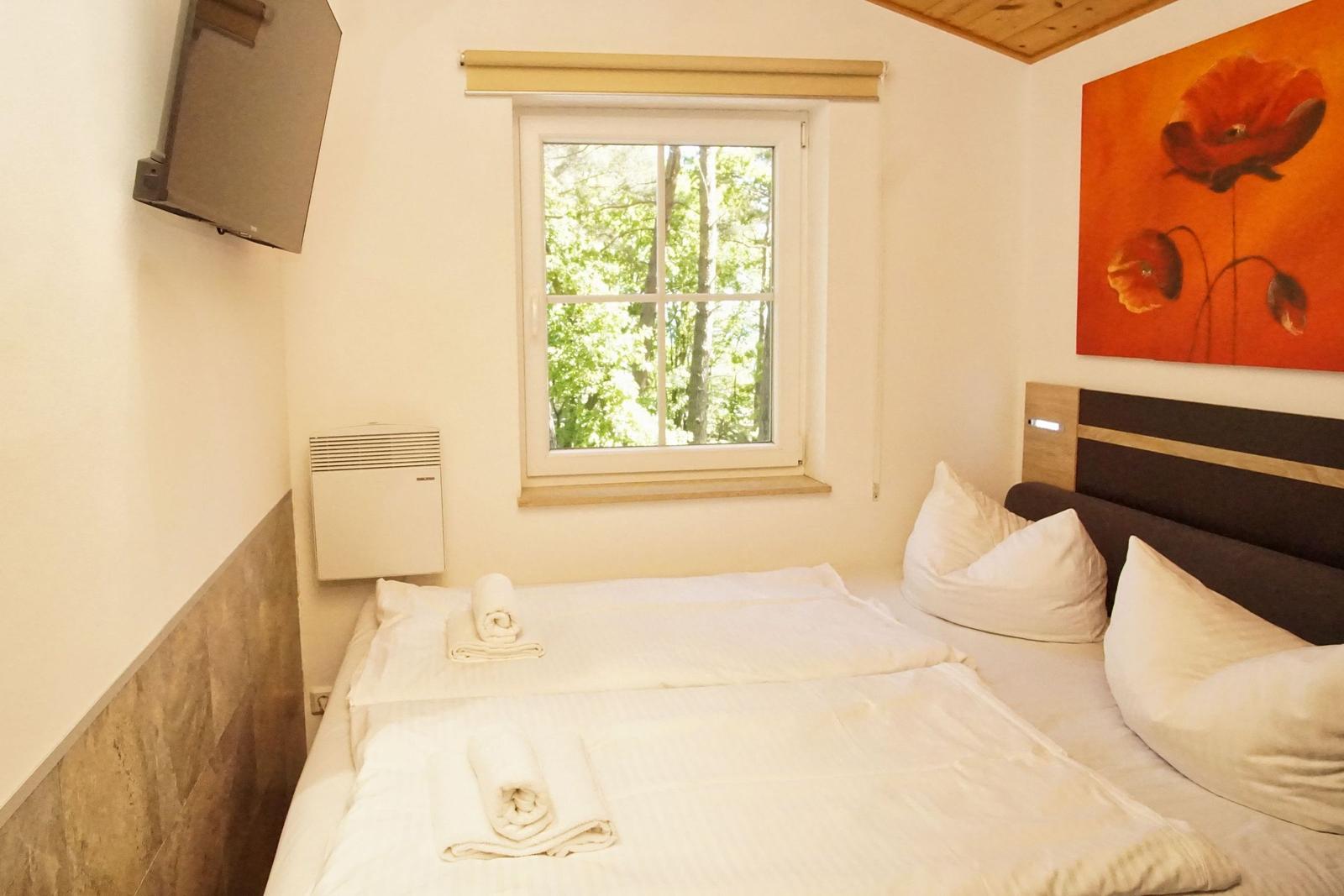 Ein Schlafzimmer mit Bett, Fenster und Wandbild. Fernseher an der Wand.