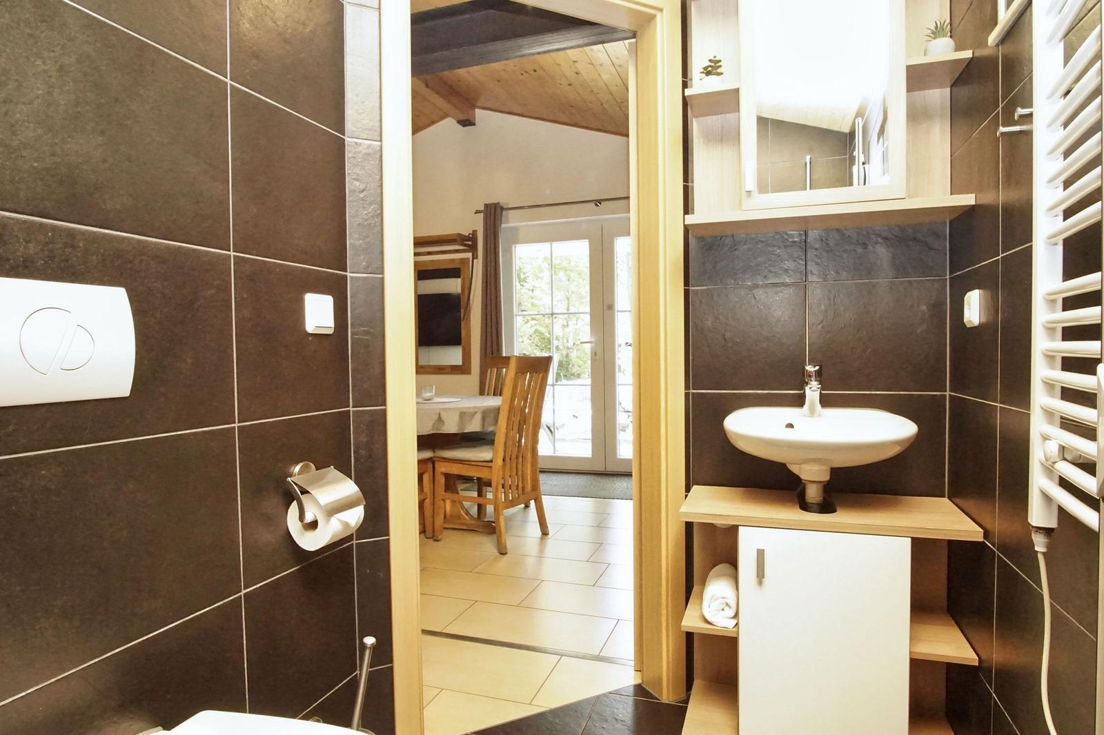Bad mit Waschbecken, Spiegelschrank und Heizkörper. Durchgang zum Essbereich mit Tisch und Stühlen.