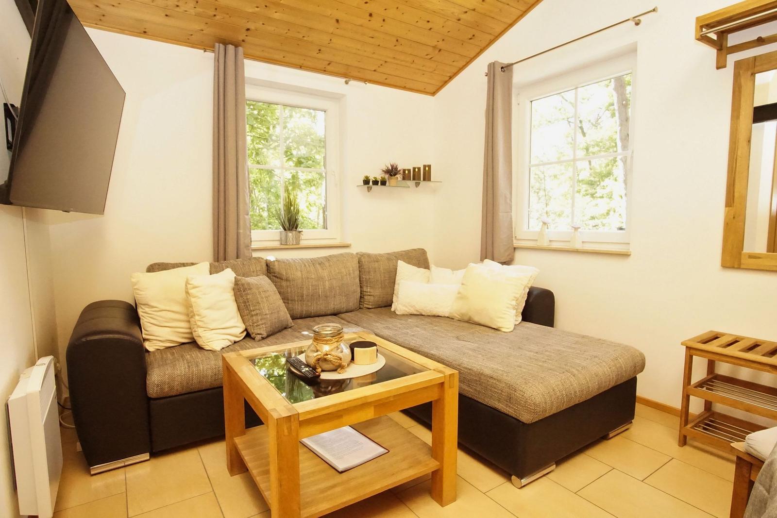 Wohnzimmer mit Sofa, Couchtisch und Fenstern zum Wald