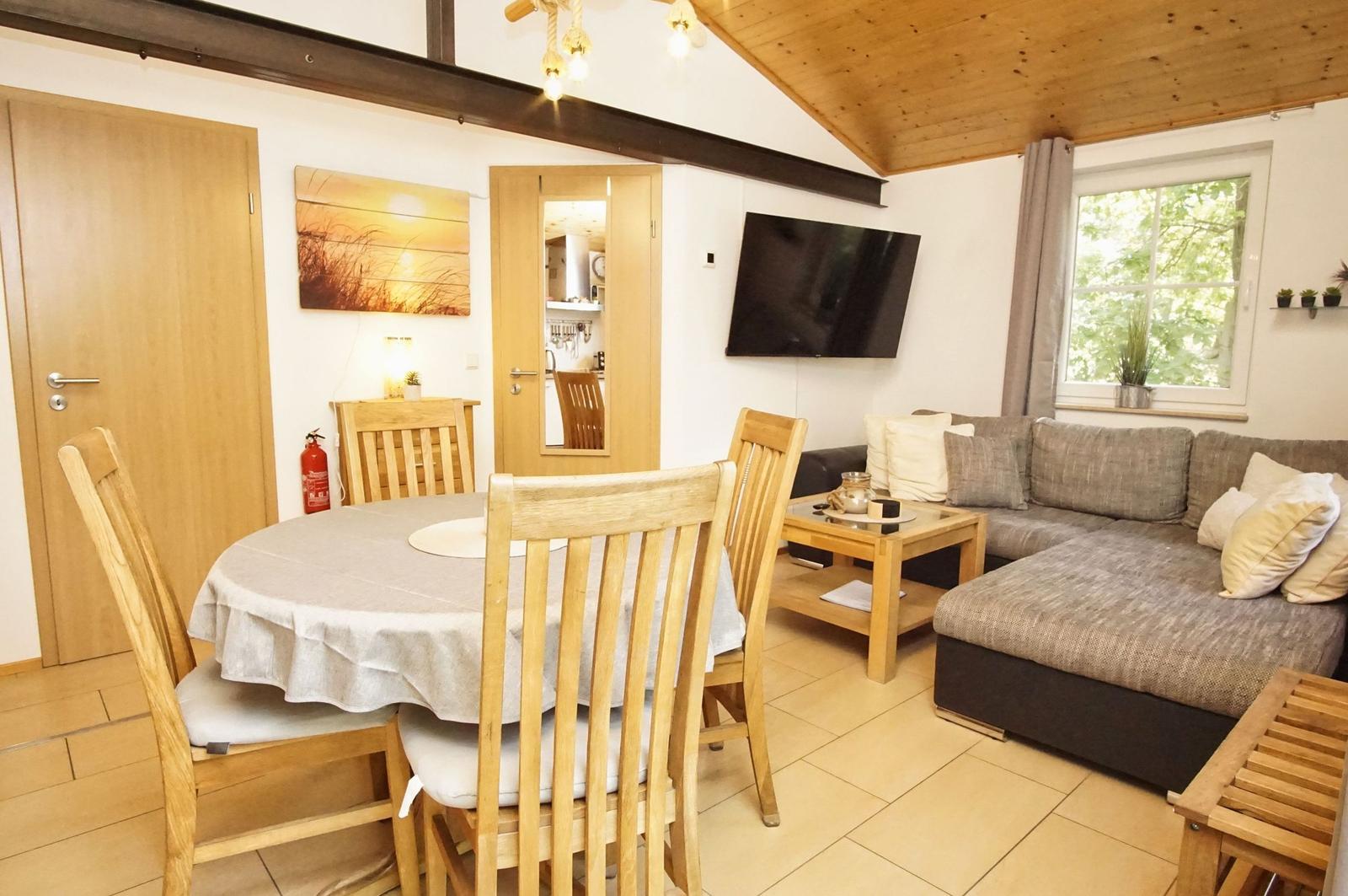 Wohn- und Essbereich mit Sofa, Esstisch und Fernseher. Holzdecke und Fenster mit Blick.
