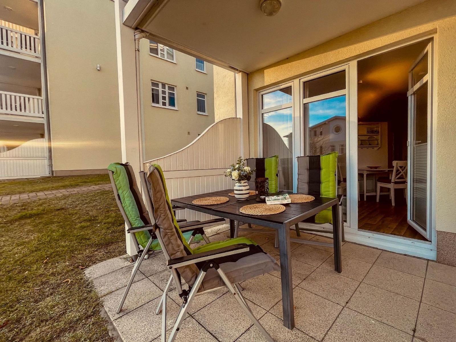 Terrasse mit Tisch, Stühlen und Blick ins Haus. Grün-weiße Polsterung.