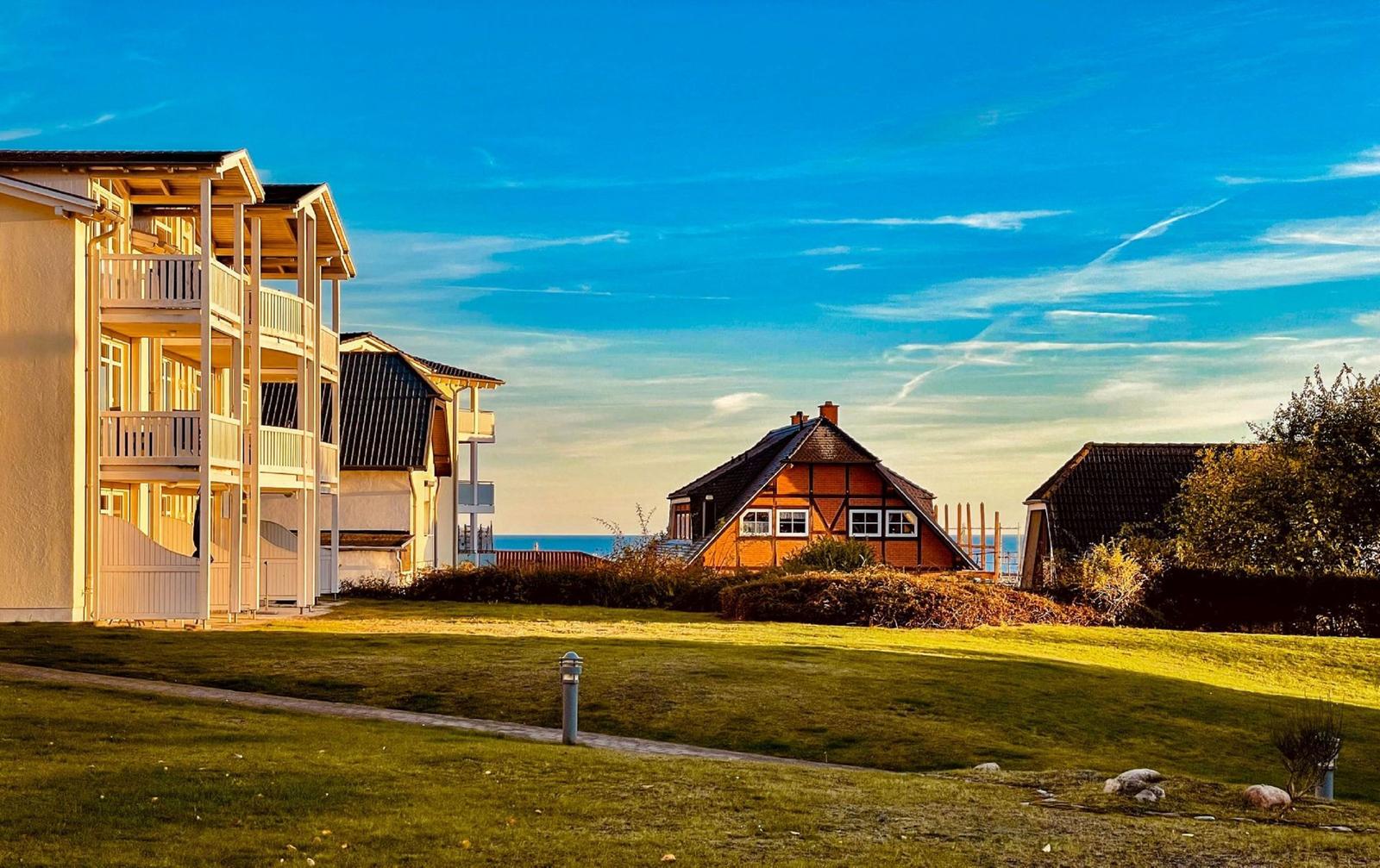 Haus mit Balkon, Grasfläche und Blick auf Meer unter blauem Himmel.