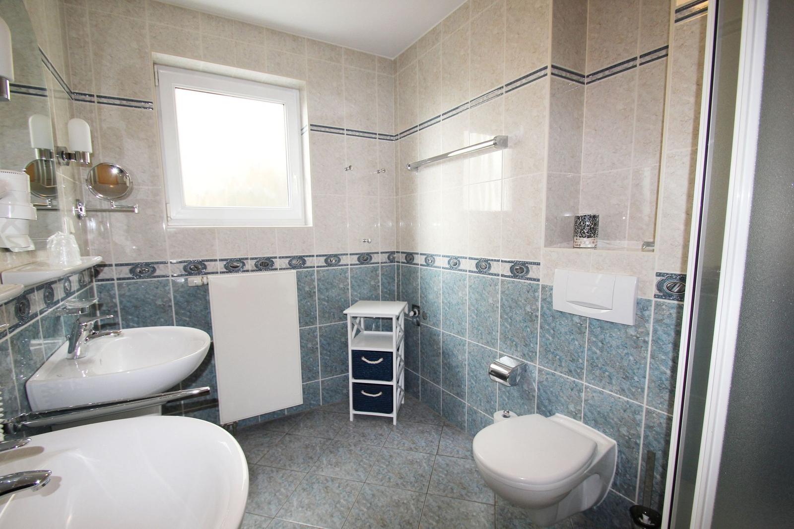 Badezimmer mit zwei Waschbecken, Toilette und Dusche. Wände mit hellen und blauen Fliesen.