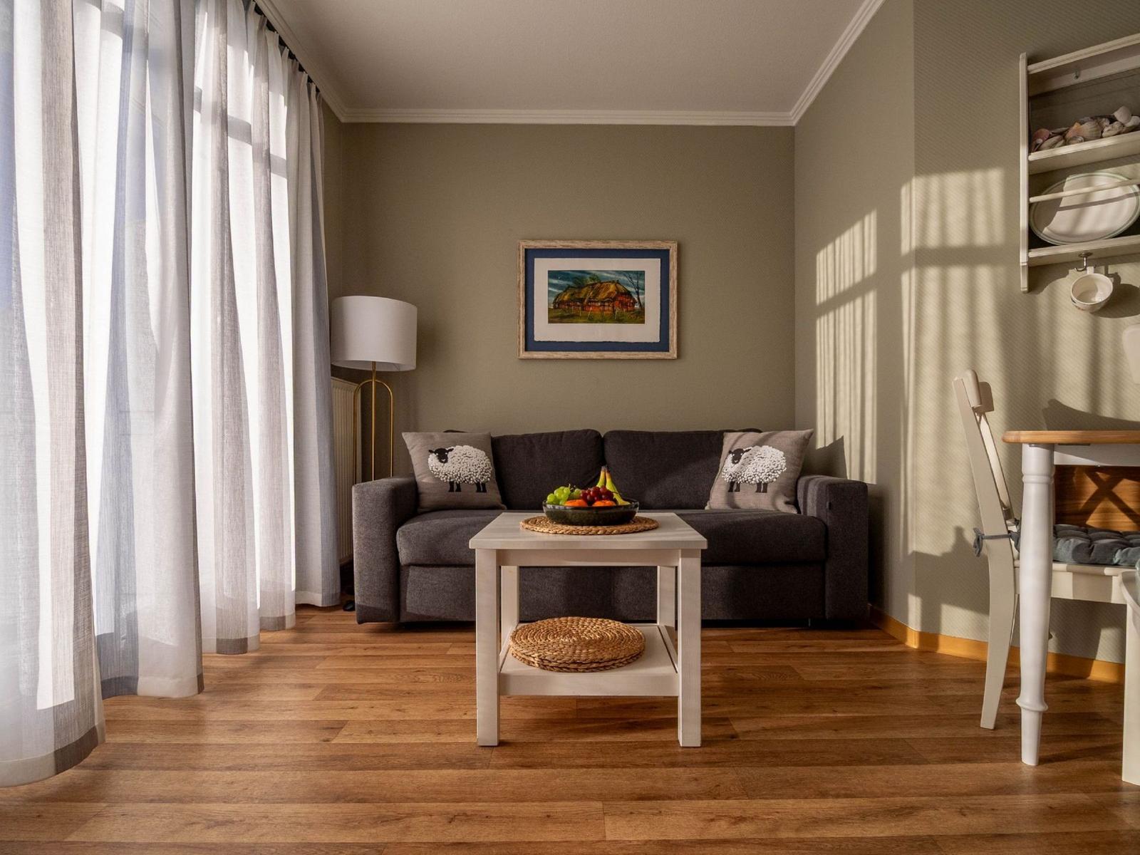 Ein Wohnzimmer mit grauem Sofa, Holzboden und einem Tisch mit Obst.