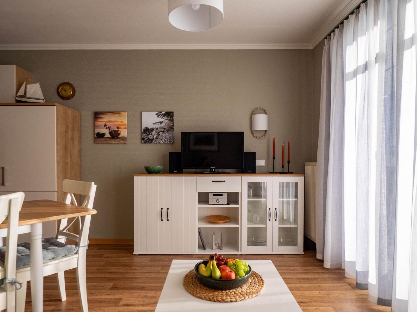 Wohnzimmer mit TV, Essbereich und Fenster mit Vorhängen.