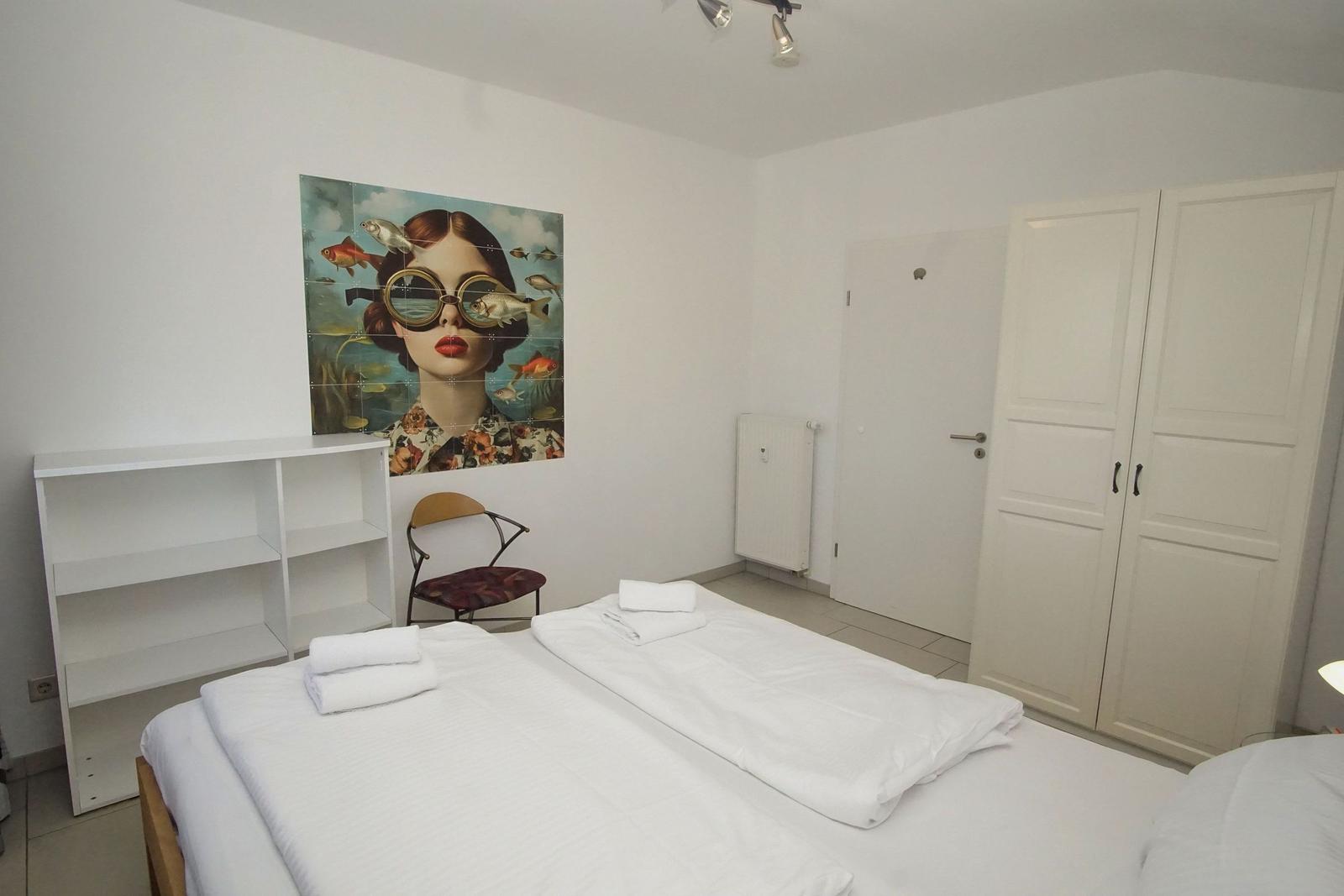 Zimmer mit Doppelbett, Wandbild, Schrank und Stuhl.