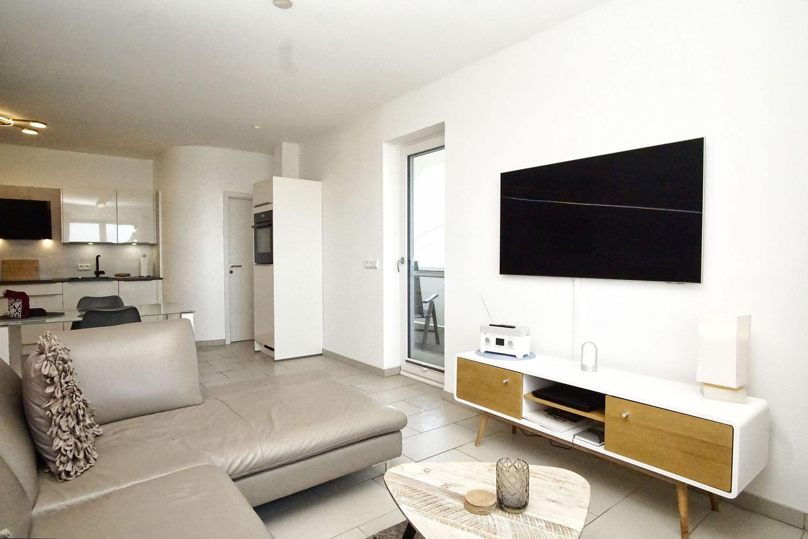 Wohnzimmer mit Sofa, TV und Küchenbereich im Hintergrund.