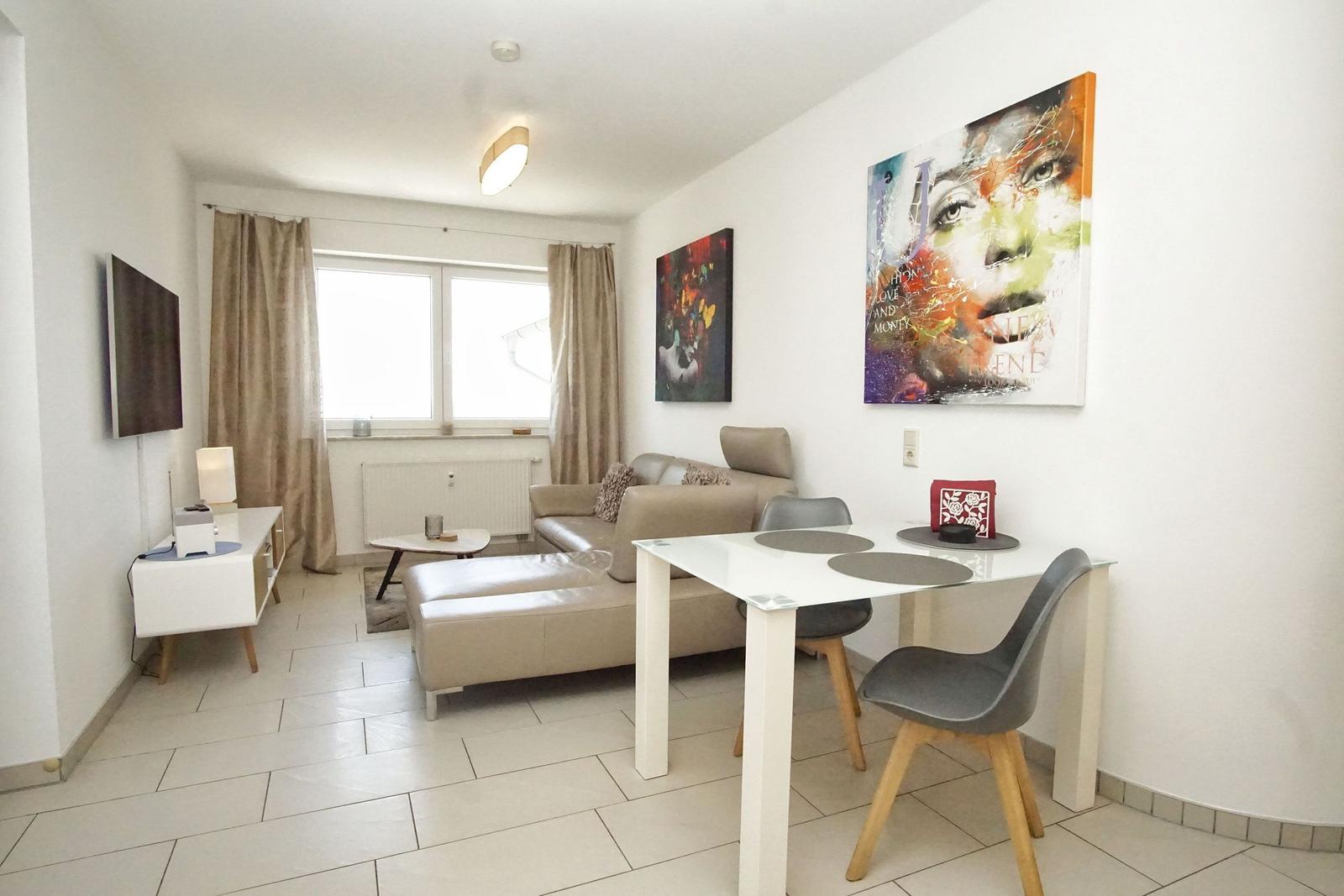 Wohnzimmer mit Sofa, Esstisch, Fernseher und Wandbildern.