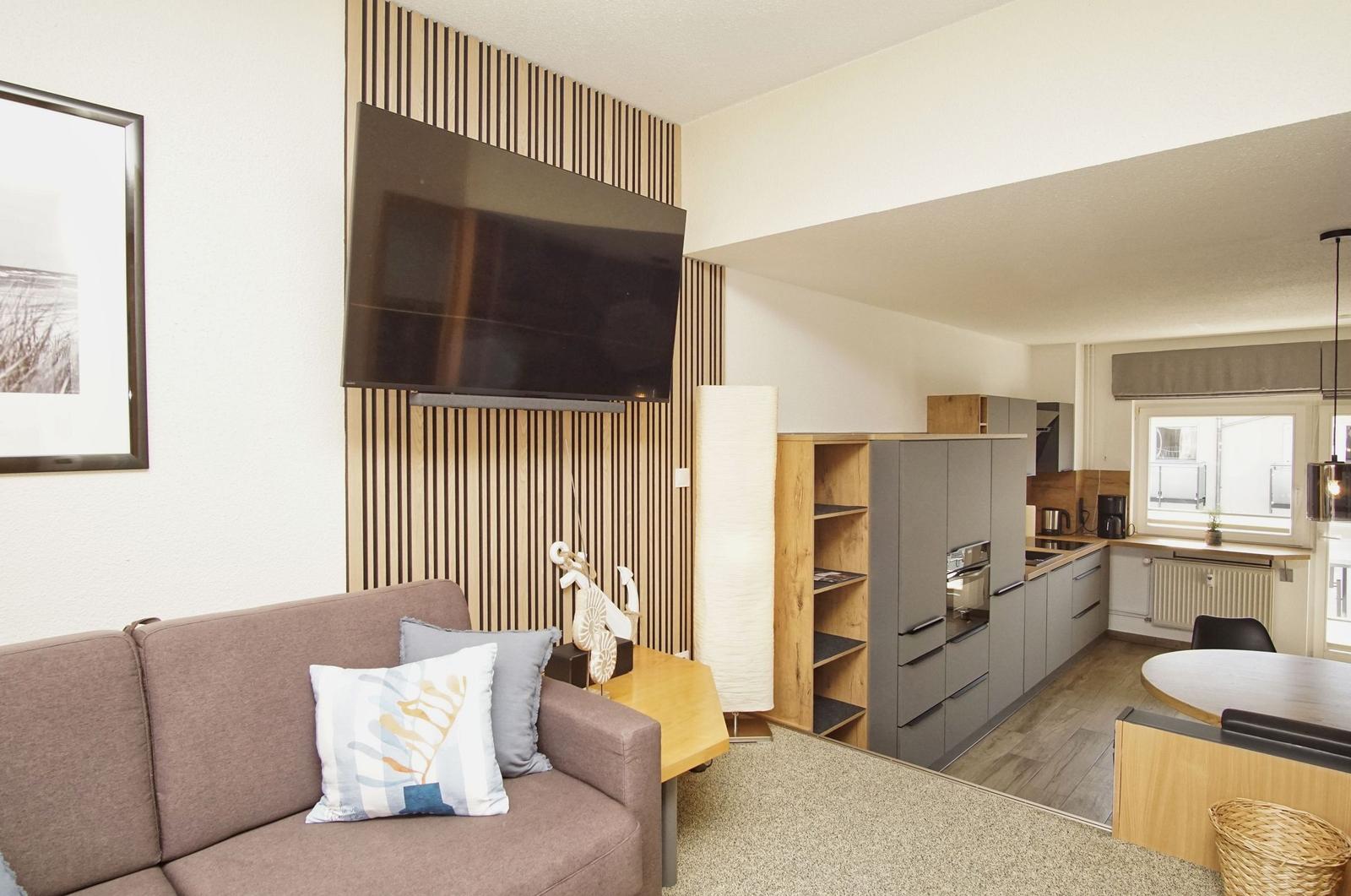 Wohnbereich mit Sofa, TV und Küchenbereich im Hintergrund.